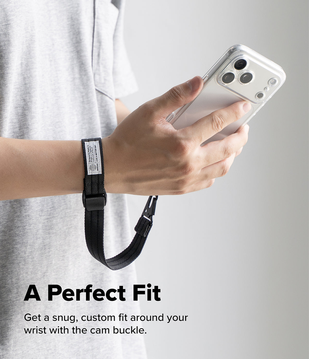 Holder Link Tactical Cam Buckle Hand Strap - A person in a light gray t-shirt holds a white smartphone while wearing a black adjustable wrist strap with a cam buckle on the wrist. Text at the bottom reads 'A Perfect Fit Get a snug, custom fit around your wrist with the cam buckle.