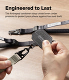 Holder Link Tactical Cam Buckle Hand Strap - A close-up of a person holding a black octagonal carabiner with a gray webbed strap, with more of the same straps laid out on a light wood surface. Text at the top reads, 'Engineered to Last' and describes the carabiner staying closed under pressure.