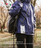 Holder Link Strap | Clear - Person wearing a clear phone case on a khaki rope crossbody strap over a blue jacket and backpack.