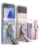 Galaxy Z Flip 6 / 5 / 4 / 3 | Hinge Cover - Three Galaxy Z Flip phones in clear cases with hinge-mounted fabric straps and metal rings.