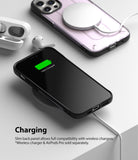 iPhone 12 / 12 Pro Case | [UX] - A black iPhone in a case charging wirelessly on a white surface with AirPods nearby.