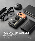 iPhone 17 Pro Max Cover | Folio Grip Wallet Magnetic - Black magnetic folio wallet case with finger strap on a desk with glasses, notebook, and pen.