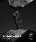 iPhone 17 Pro Case | Rugged Gear - Black camo phone case suspended between two dark, jagged rocks against a moody background.