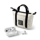 Mini Pouch | Tote Bag - A cream-colored mini canvas tote bag with black straps and a white wireless earbud case with one earbud.