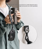 Mini Pouch | Sling Bag - A person holds a tumbler with a branded black strap attached to a small black pouch via a carabiner.