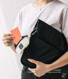 Mini Pouch | Sling Bag - A person holding a black sling bag with a small beige pouch attached by a carabiner, inserting a card.