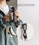 Mini Pouch | Sling Bag - A person holding a tumbler with a small beige pouch attached to the handle via a branded strap.