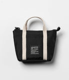 Mini Pouch | Tote Bag - Black mini tote bag with beige handles and a square branded patch on a light gray background.