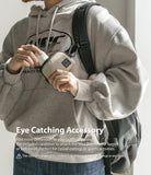 Mini Pouch | Half-Pocket - Person in a grey hoodie attaching a beige mini pouch to a backpack strap with a carabiner.