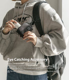 Mini Pouch | Half-Pocket - Person in a grey hoodie holding a black mini pouch attached to a backpack strap with a carabiner.