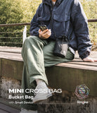Mini Cross Bag | Bucket Bag - Person sitting on a bench wearing a black drawstring bucket bag crossbody.