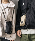 Mini Cross Bag | Bucket Bag - Two people wearing black and beige drawstring bucket bags with rope straps over outdoor jackets.