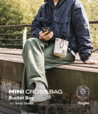 Mini Cross Bag | Bucket Bag - Person sitting on a bench wearing a beige drawstring bucket bag crossbody.