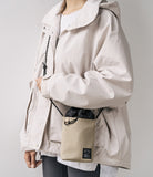 Mini Cross Bag | Bucket Bag - Person wearing a beige jacket and a small beige bucket bag with a black drawstring closure.