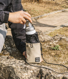 Mini Cross Bag | Bucket Bag - A person placing a water bottle into a beige and black drawstring bucket bag with a shoulder strap.