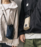 Mini Cross Bag | Bucket Bag - Two people wearing navy and beige drawstring bucket bags with rope straps over jackets.