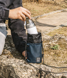 Mini Cross Bag | Bucket Bag - A person placing a water bottle into a navy blue drawstring bucket bag with a rope strap.