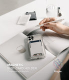 Card Holder | Magnetic Slot - A white magnetic card holder attached to a clear phone case resting on an open notebook.