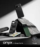 Google Pixel 9a Case | Onyx - Three textured phone cases and a smartphone arranged on jagged rocks against a dark background.