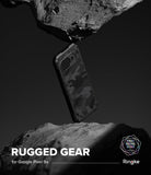 Google Pixel 9a Case | Rugged Gear - Camouflage phone case suspended between two jagged rocks against a dark background.