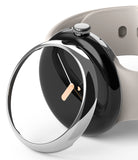Google Pixel Watch 41mm | Bezel Styling - A silver metallic bezel ring hovering above a black Pixel Watch with a beige band.