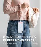 Holder Link Puffer | Hand - A person wearing a pink puffer wrist strap attached to a clear phone case hanging against blue jeans.