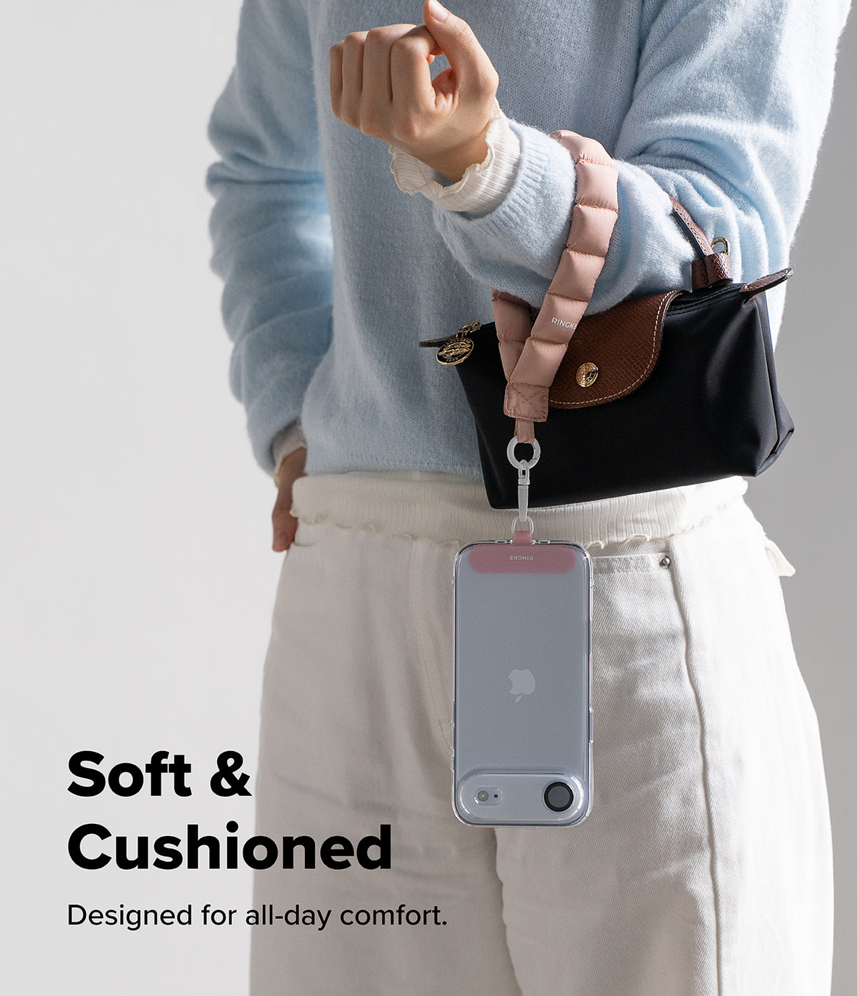 Holder Link Puffer | Hand - A person wearing a soft, pink puffer wrist strap attached to a small handbag and a clear phone case.
