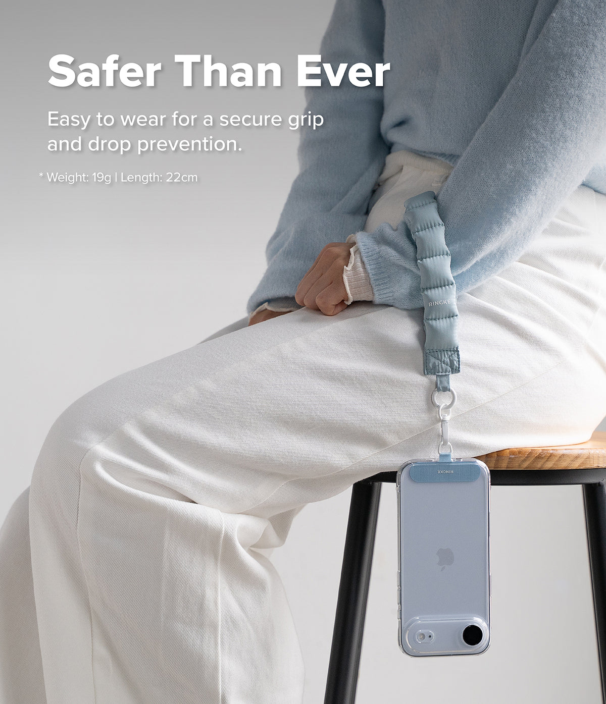 Holder Link Puffer | Hand - A person wears a light blue quilted wrist strap attached to a smartphone hanging from their hand.