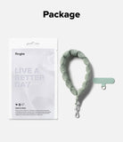 Holder Link Puffer | Hand - Sage green puffer wrist strap with a matching adhesive anchor tab and Ringke retail packaging.