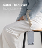 Holder Link Puffer | Hand - Person wearing a beige quilted puffer wrist strap attached to a clear phone case while sitting.