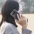 Paracord Lanyard Wrist Strap [2 Pack] - Woman holding a smartphone with a gray checkered paracord wrist strap attached.