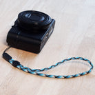 Paracord Lanyard Wrist Strap [2 Pack] - Black camera attached to a blue, white, and black patterned paracord wrist strap.