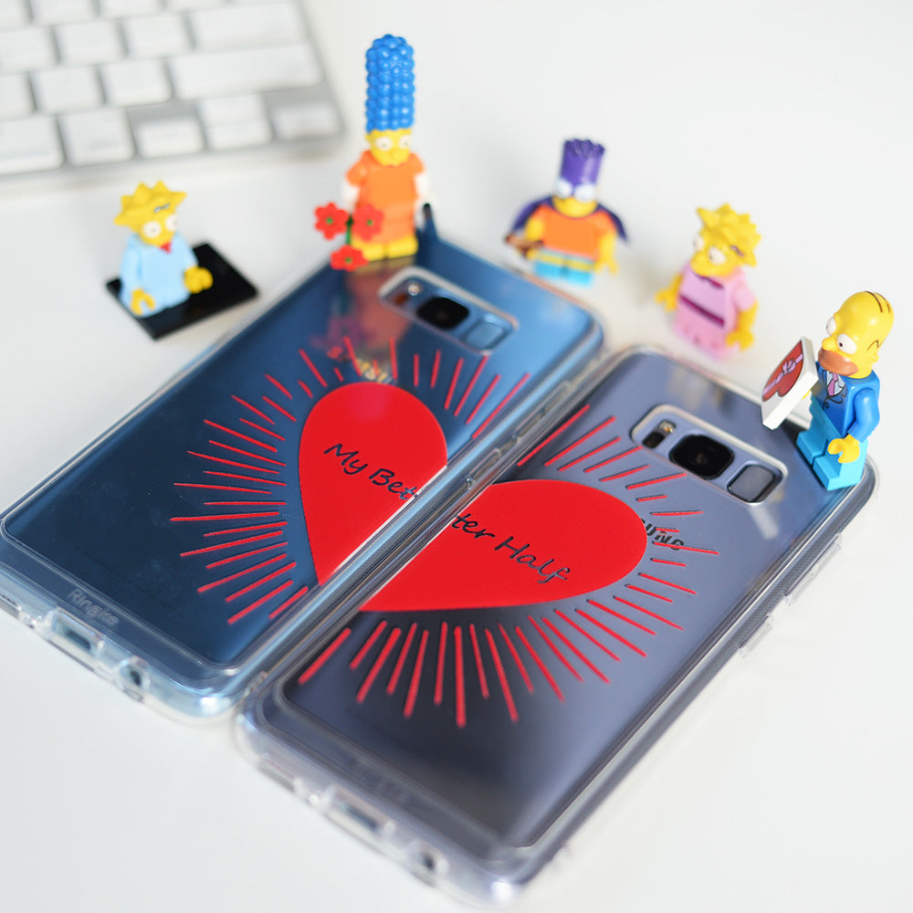 Galaxy S8 Case | Fusion Deco - Two clear phone cases featuring a split red heart design with Simpsons minifigures nearby.