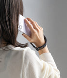 Dual Hand Slim Strap - A person holding a white smartphone to their ear with a black wrist strap secured around their hand.