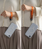 Dual Hand Slim Strap - A person wearing an orange wrist strap attached to a clear phone case with a MagSafe ring.