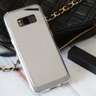 Galaxy S8 Plus Case | Mirror - Reflective silver phone case resting on a white surface next to a black quilted handbag.
