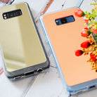 Galaxy S8 Plus Case | Mirror - Two reflective mirror-finish phone cases in silver and rose gold on a white wooden surface.
