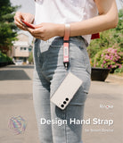 Hand Strap | Basic - A person wearing a pink fabric wrist strap attached to a smartphone in a clear case.
