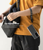 Hand Strap | Lettering - Person wearing a black Ringke branded wrist strap attached to a smartphone hanging from their arm.