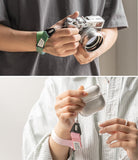 Hand Strap | Basic - A green strap on a camera and a pink strap on an earbud case, both worn around the wrist.
