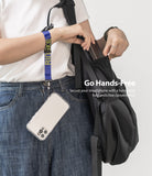 Hand Strap | Lettering - A person wearing a blue patterned wrist strap attached to a smartphone hanging by their side.