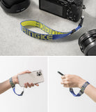 Hand Strap | Lettering - Blue and yellow Ringke branded wrist strap attached to a camera and held by a hand with a phone.