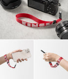 Hand Strap | Lettering - Red wrist strap with white Ringke logo attached to a camera and held by a hand with a smartphone.