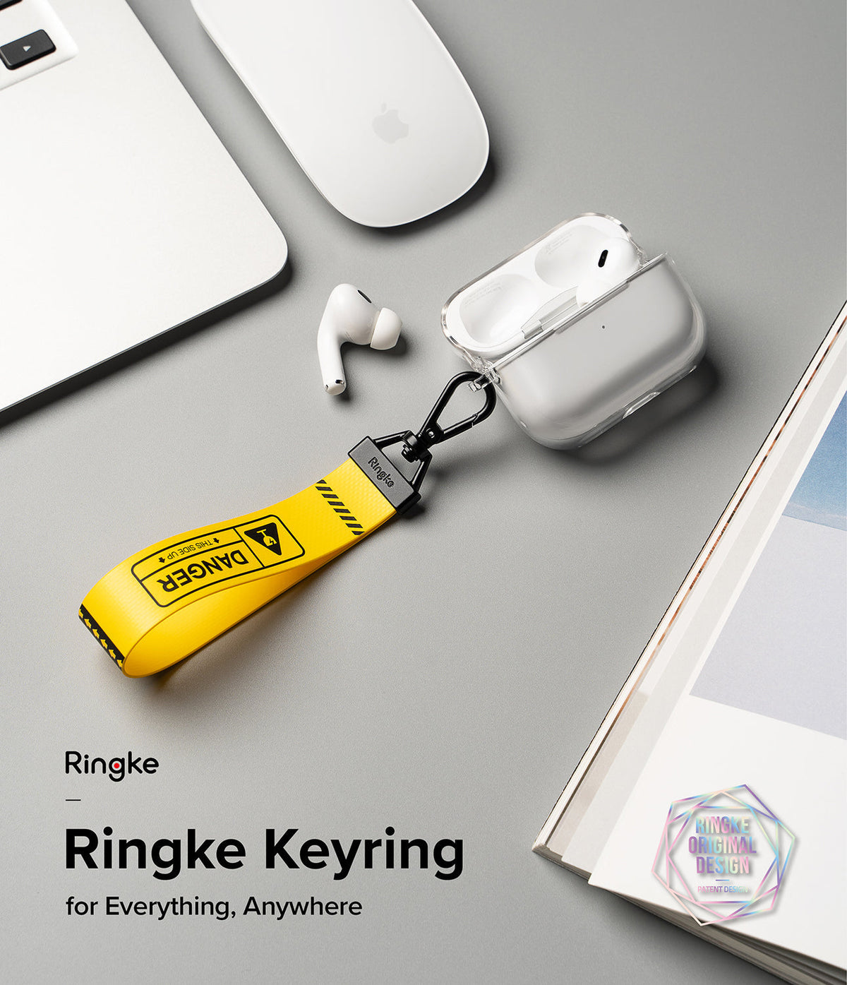 Key Ring Strap | Danger - Yellow strap with black Danger text attached to a clear AirPods case on a grey desk.