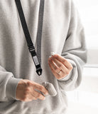 Design Lanyard Strap - Person wearing a black branded lanyard attached to a beige earbud case while holding an earbud.