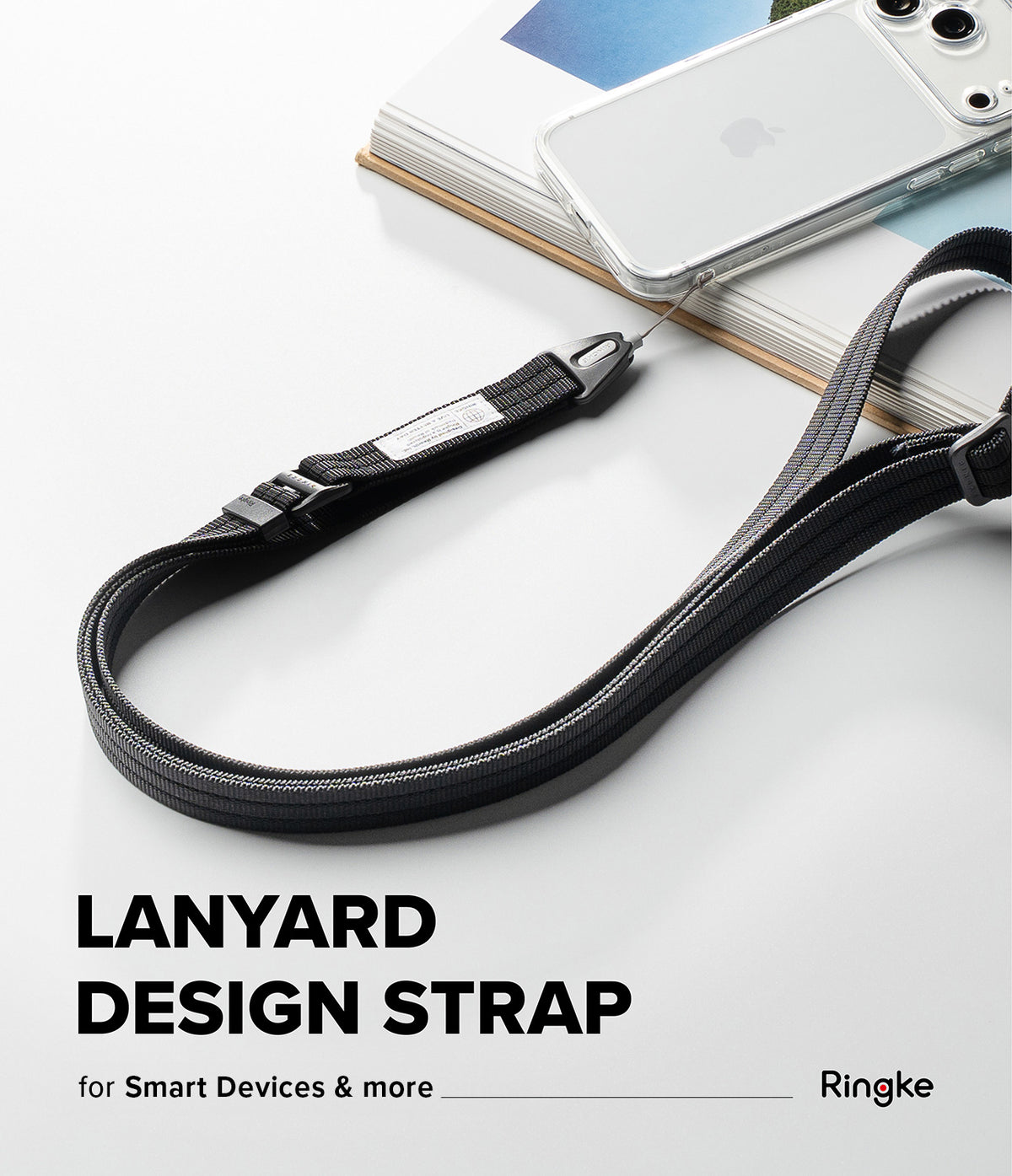 Design Lanyard Strap - A black adjustable lanyard design strap with white stitching and a silver metal clip, shown draped over stacked books with a white smartphone resting on top. Text at the bottom reads 'LANYARD DESIGN STRAP for Smart Devices & more Ringke'.