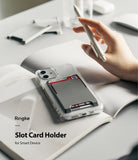 Card Holder | Slot [3 Cards] - Grey adhesive card holder on a clear phone case holding three cards, resting on an open book.