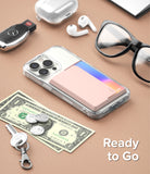 Card Holder | Side Slot - Pink card holder attached to a clear phone case, surrounded by personal items on a tan surface.