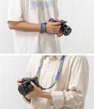 Shoulder Strap | Lettering - Blue camera strap with yellow lettering worn as a wrist loop and a neck strap on a mirrorless camera.