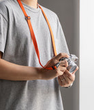 Shoulder Slim Strap - Person wearing a bright orange slim camera strap around their neck while holding a silver mirrorless camera.